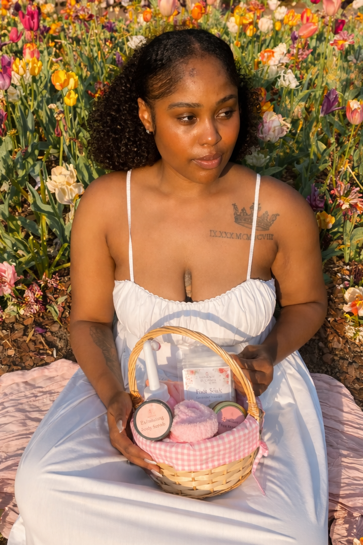 Woman sitting in a garden holding a basket with postpartum essentials, surrounded by colorful flowers.
